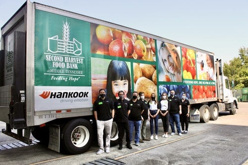A group of people wearing masks stand in front of a large Second Harvest Food Bank truck decorated with images of food and faces. The truck has logos for Second Harvest and Hankook.