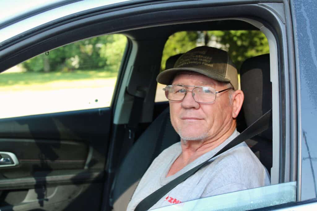 Larry, an older man managing diabetes while facing food insecurity, sits in the driver’s seat of his car. Larry relies on support from Second Harvest to access healthy, low-sugar foods, which help him manage his condition.