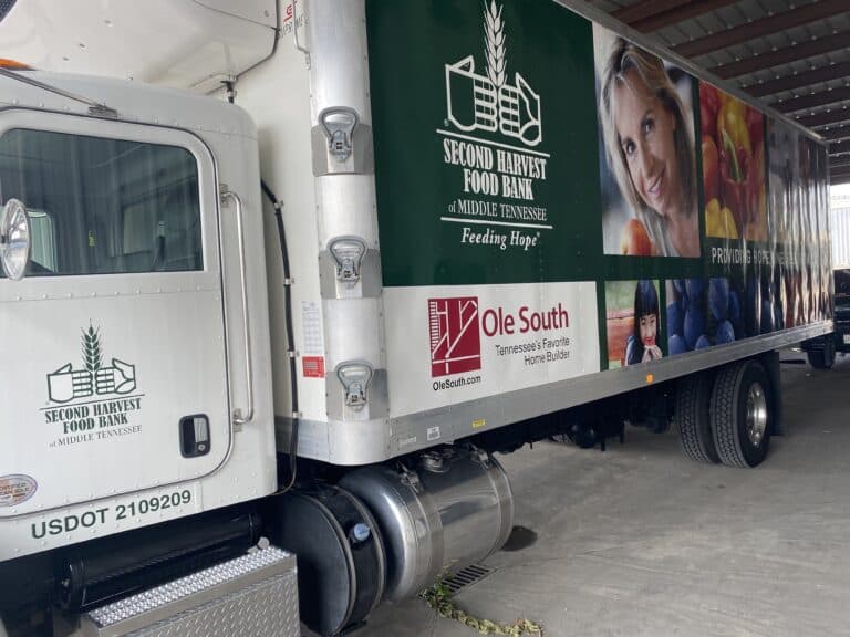 A Second Harvest Food Bank of Middle Tennessee truck with images of food and people on its side, parked under a shelter; sponsor logos and “Feeding Hope” slogan are visible.