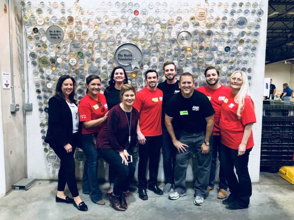 A group of nine people, some in red shirts and others in casual or business attire, pose smiling in front of a wall decorated with many round plaques in a modern indoor setting.