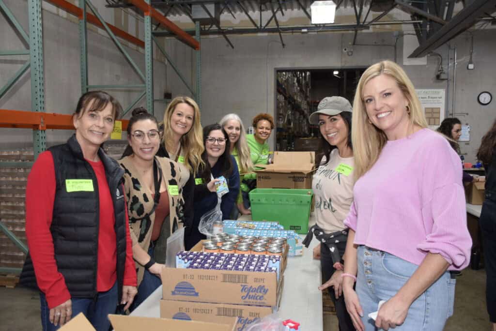 Kim Smith (far left) with coworkers and friends volunteering at Second Harvest’s annual Galentine’s event, showing how to multiply your impact by inspiring others to serve.