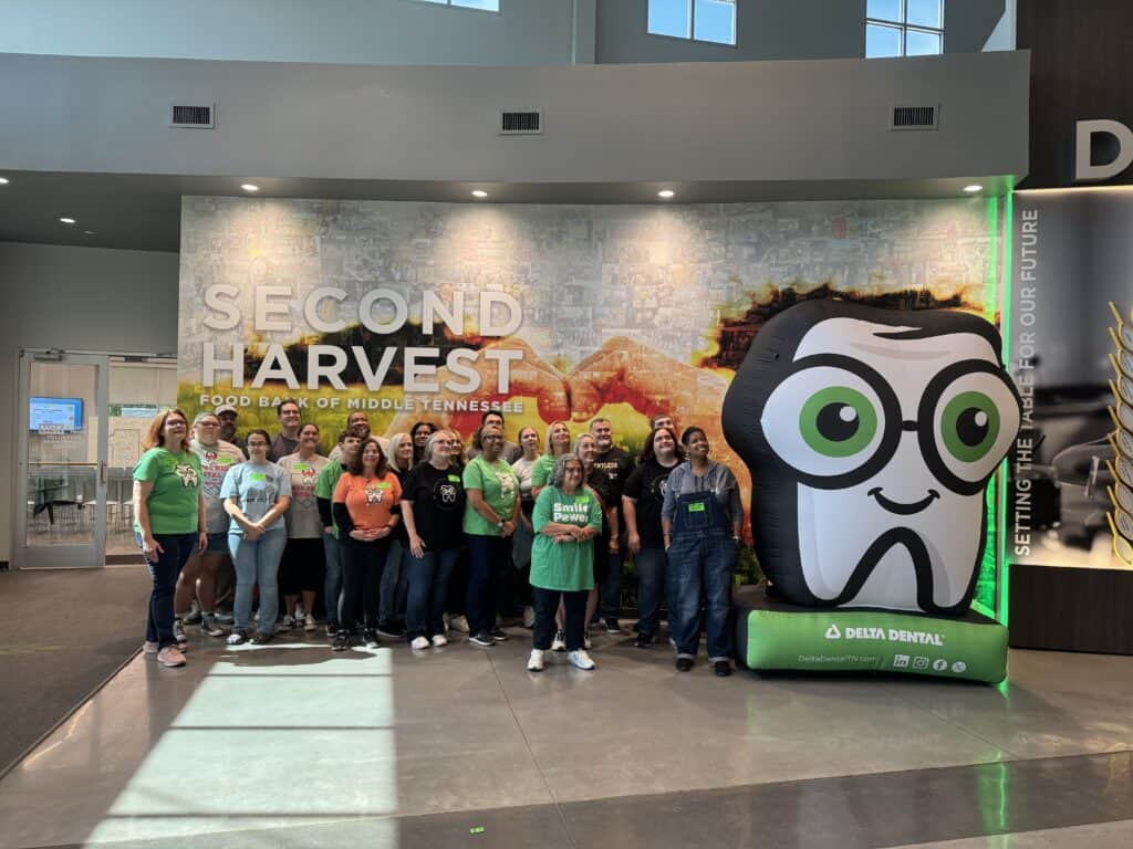 Delta Dental Creates Change with the Power of ONE. A group of people pose for a photo inside the Second Harvest Food Bank of Middle Tennessee, standing next to a large green and white inflatable Delta Dental mascot.