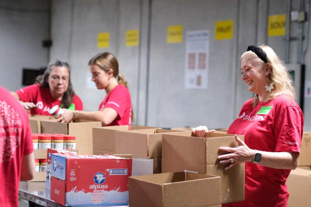 Jackson Invests in a Brighter Future at Second Harvest. Volunteers in red shirts pack food boxes at Second Harvest Food Bank, smiling as they sort pantry staples and prepare supplies for neighbors in need.For 14 years, Jackson National has partnered with Second Harvest to fight hunger, contributing $680,200, volunteering regularly, and supporting the Senior Nutrition Program since 2010.