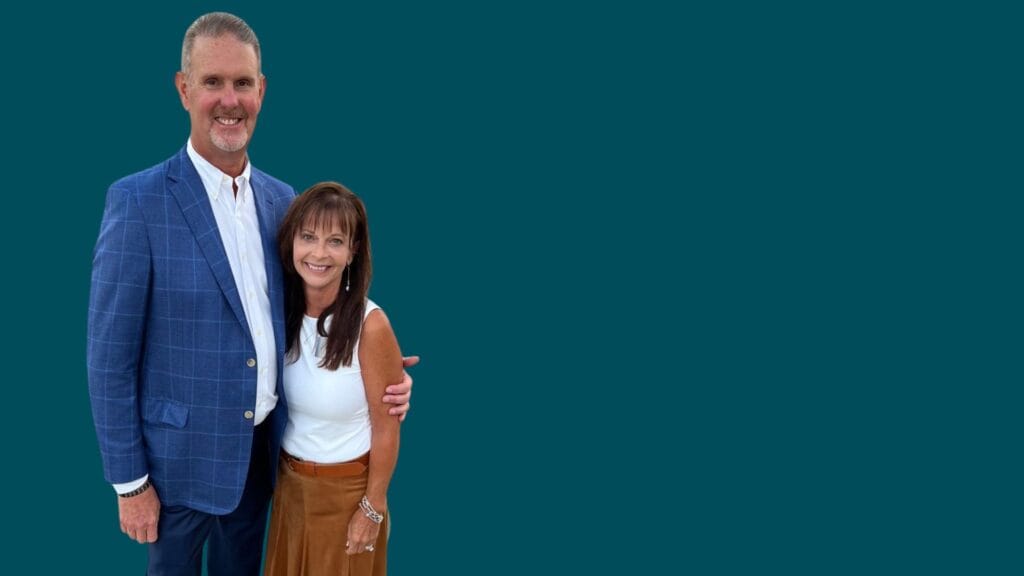A smiling man in a blue blazer and white shirt stands with his arm around a smiling woman in a white top and brown skirt, both posed against a plain teal background, embodying the spirit of How to Multiply Your Impact through connection.