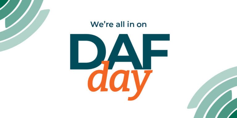 Text graphic with the words Were all in on DAF day in teal and orange letters, with abstract green circular designs in the top left and bottom right corners on a white background.