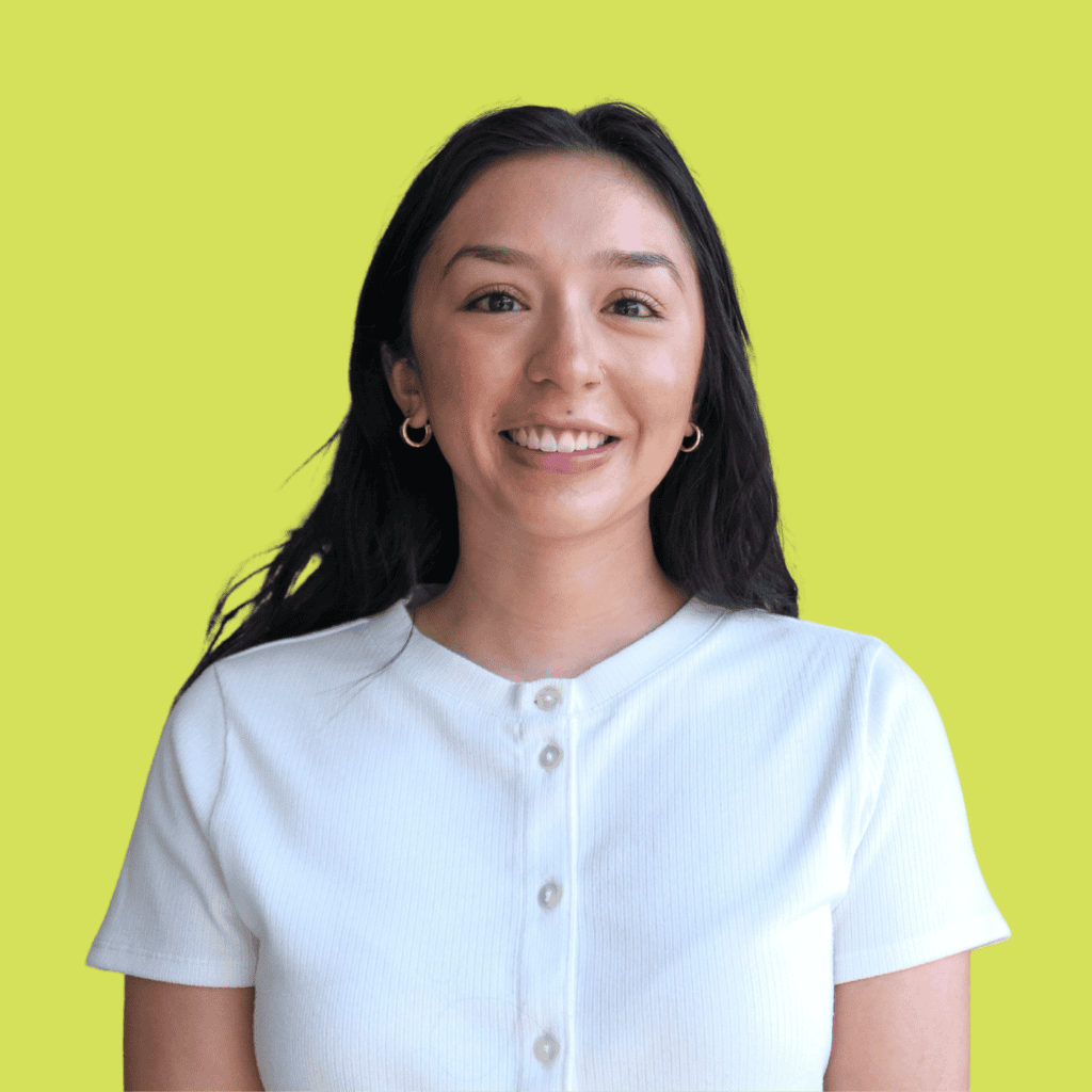 A woman with long dark hair wearing a white short-sleeve shirt and gold hoop earrings smiles in front of a plain yellow background.