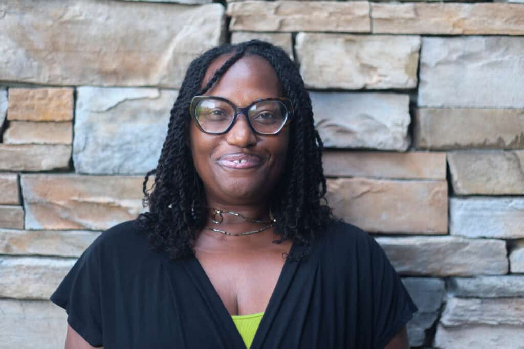 Second Harvest Food Bank of Middle Tennessee transportation coordinator smiling in front of a stone wall during a Women in Hunger Relief feature for International Women’s Day.