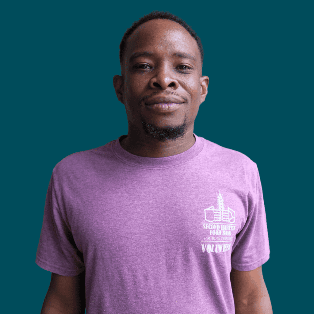 A man stands against a solid teal background, wearing a purple Second Harvest Food Bank Volunteer t-shirt. He is looking at the camera with a neutral expression.