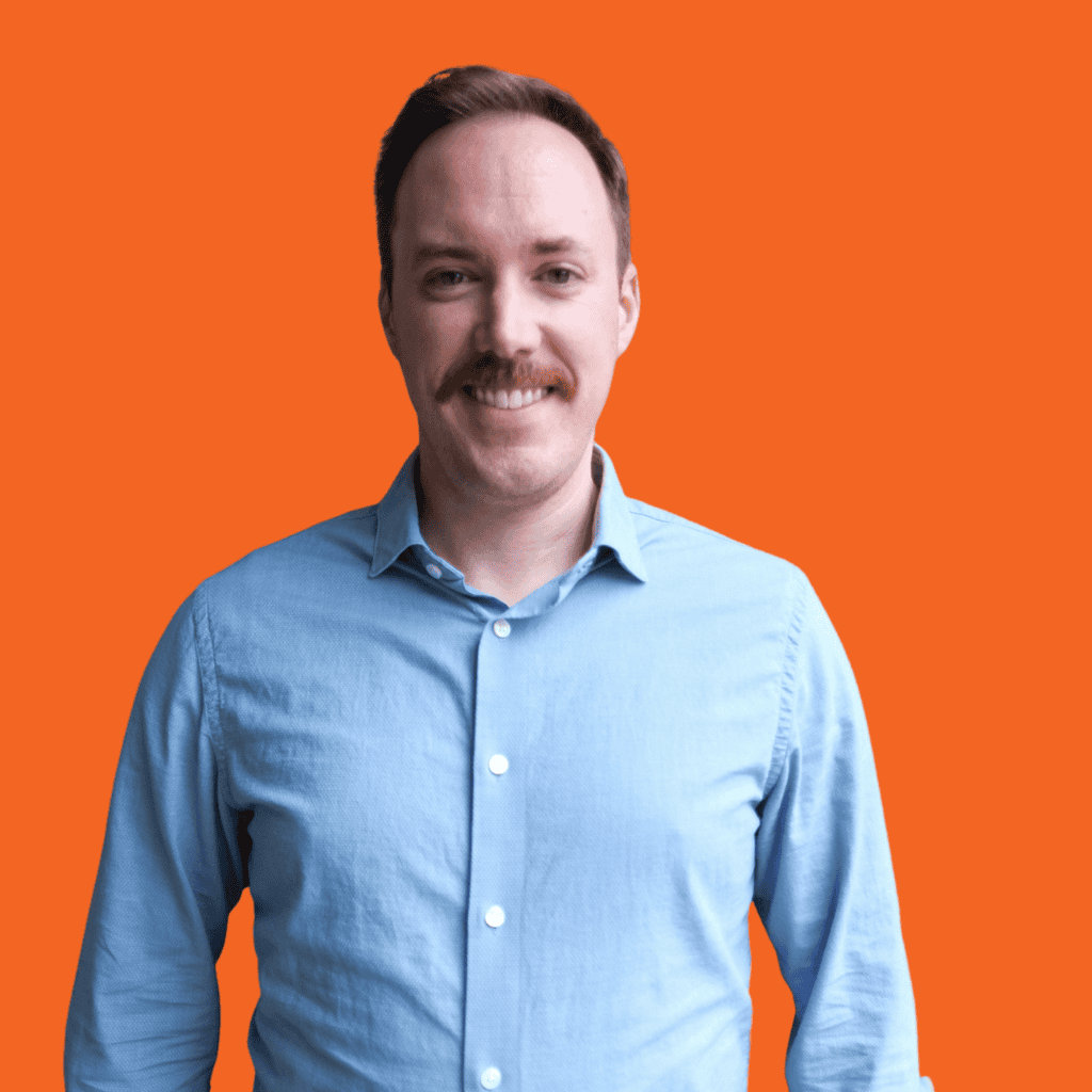 A person wearing a light blue button-up shirt is smiling, standing against a solid bright orange background.
