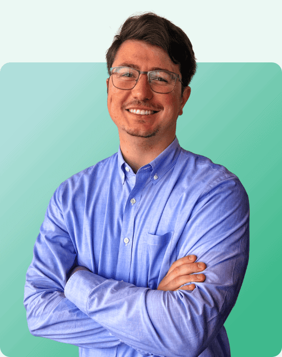 A man wearing glasses and a light blue button-up shirt stands smiling with his arms crossed in front of a teal gradient background.