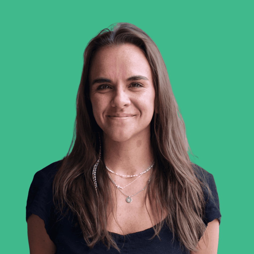 Woman with long brown hair wearing a black top and layered necklaces, smiling in front of a solid teal background.
