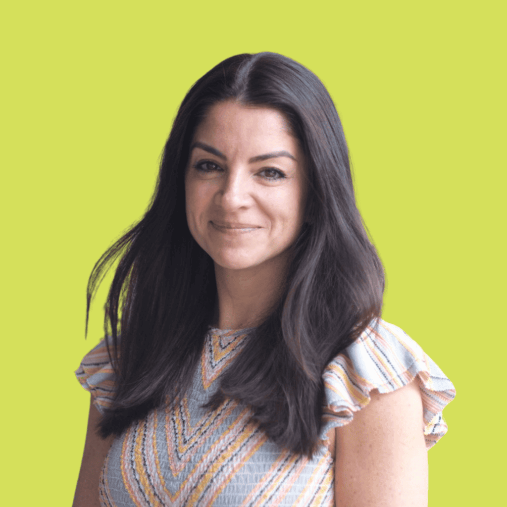 A woman with long dark hair and a patterned short-sleeve top smiles in front of a solid yellow-green background.