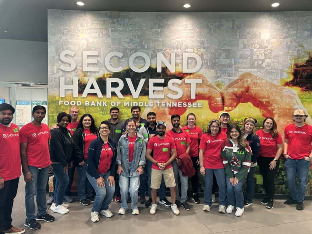 A group of people wearing red Jackson t-shirts pose in front of a Second Harvest Food Bank of Middle Tennessee wall inside a building.
